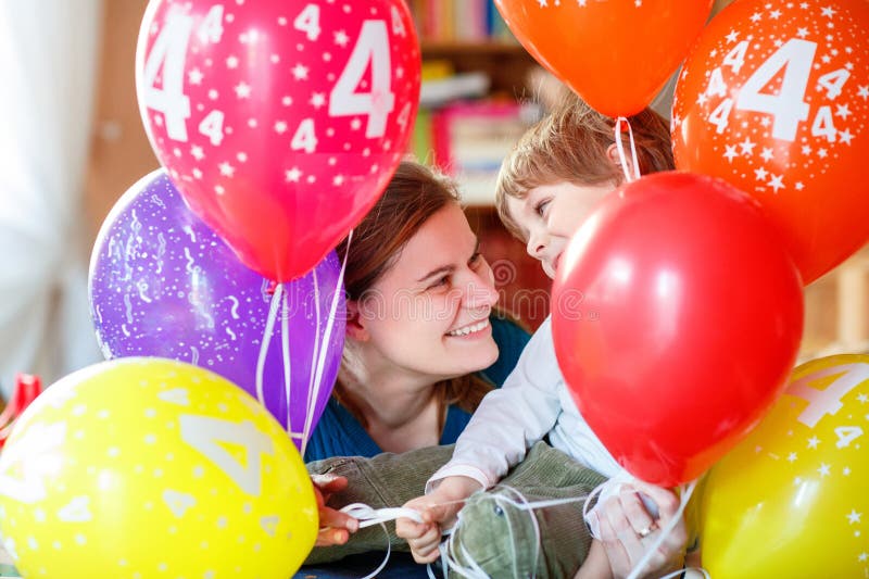 Băiețel fericit și mama sărbătorește 4 aniversare cu baloane colorate. Adorabil copil și tineri femeie îmbrățișare și având royalty free stock image
