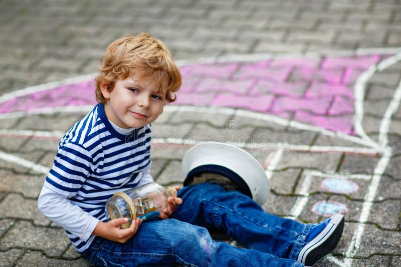 Băiețel mic ca pirat pe navă sau barcă cu pânze pictură cu cretă colorată pe asfalt. Timp liber creativ pentru copii stock photography