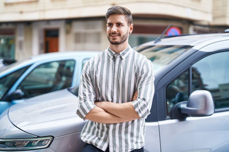 Bărbat caucazian tânăr care zâmbește încrezător în picioare cu mașina cu brațe încrucișate la stradă royalty free stock photo