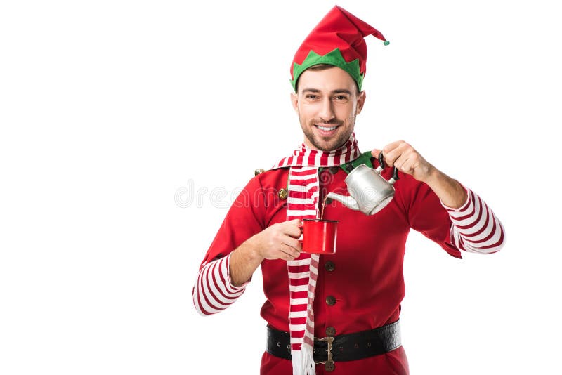Bărbat fericit în costum elf de Crăciun cu ceainicul din metal turnând ceai în cupă și uitându-se la camera izolată royalty free stock images