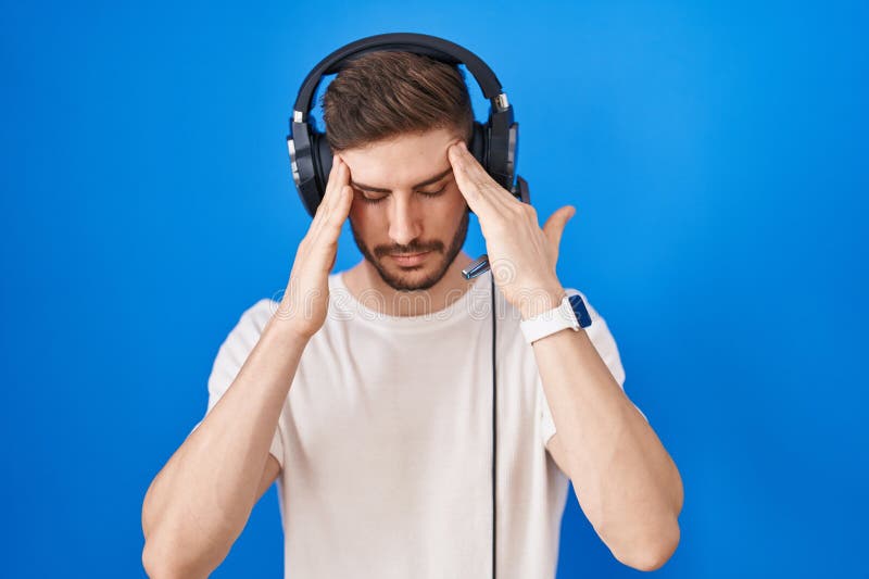 Bărbat hispanic cu barbă ascultând muzică purtând căști cu mâna pe cap, pentru că stresul royalty free stock photo