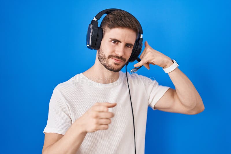 Bărbat hispanic cu barbă ascultând muzică purtând căști zâmbind vorbind la telefon și arătând spre tine stock image