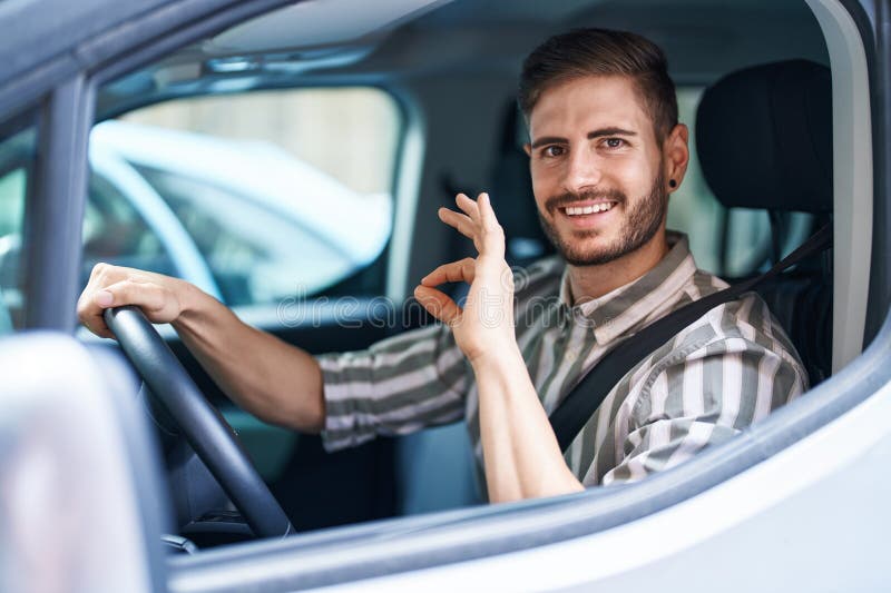 Bărbat hispanic cu barbă conducând o mașină care face un semn bun cu degetele zâmbind prietenos, gestând un simbol excelent stock photos