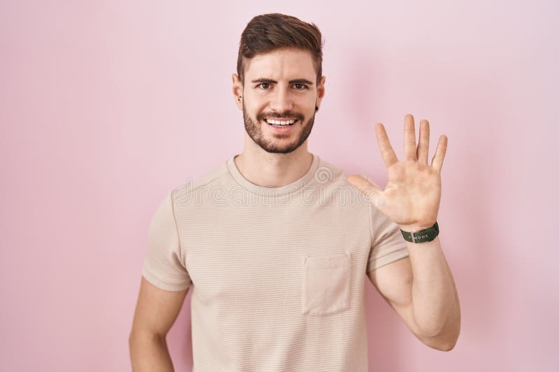 Bărbat hispanic cu barbă în picioare pe fond roz arătând și arătând cu degetul numărul cinci în timp ce zâmbea încrezător și royalty free stock image