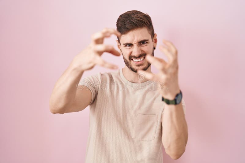 Bărbat hispanic cu barbă în picioare pe fond roz strigând frustrat cu mâinile de furie încercând să sugrume urlând nebun