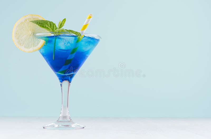 Băutură glaciară albastră rece de vară cu cuburi de gheață, felie de lămâie, mentă verde de paie galbenă, în sticlă de vin elegant stock images