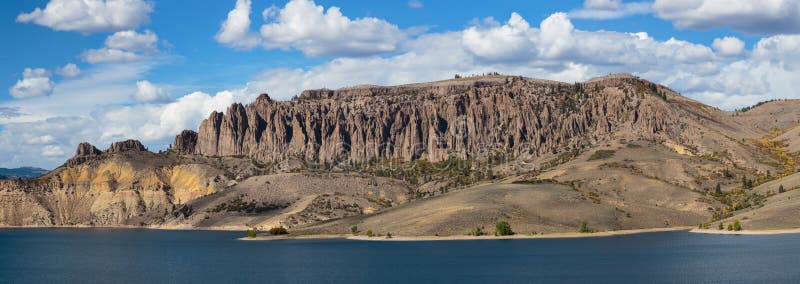 The Cliffs of Blue Mesa as viewed across a large reservoir with puffy white clounds in a blue sky. The Cliffs of Blue Mesa as viewed across a large reservoir with puffy white clounds in a blue sky.