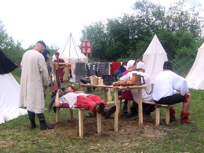 Caballeros de la gente en los trajes medievales que descansan sobre la tierra cerca de las tiendas antes de la batalla de los Vik imágenes de archivo libres de regalías Caballeros de la gente en los trajes medievales que descansan sobre la tierra cerca de las tiendas antes de la batalla de los Vik imágenes de archivo libres de regalías