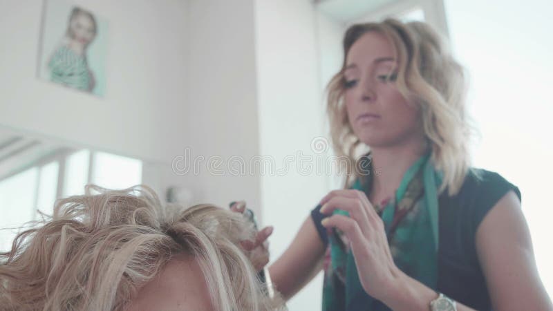 Cabeleireiro corta e penteia o cabelo com secador para senhora loira