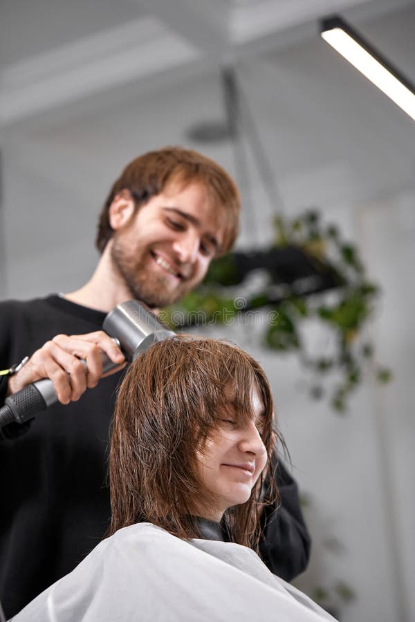 Cabeleireiro seca e modela o cabelo com um secador de cabelo no salão de  beleza