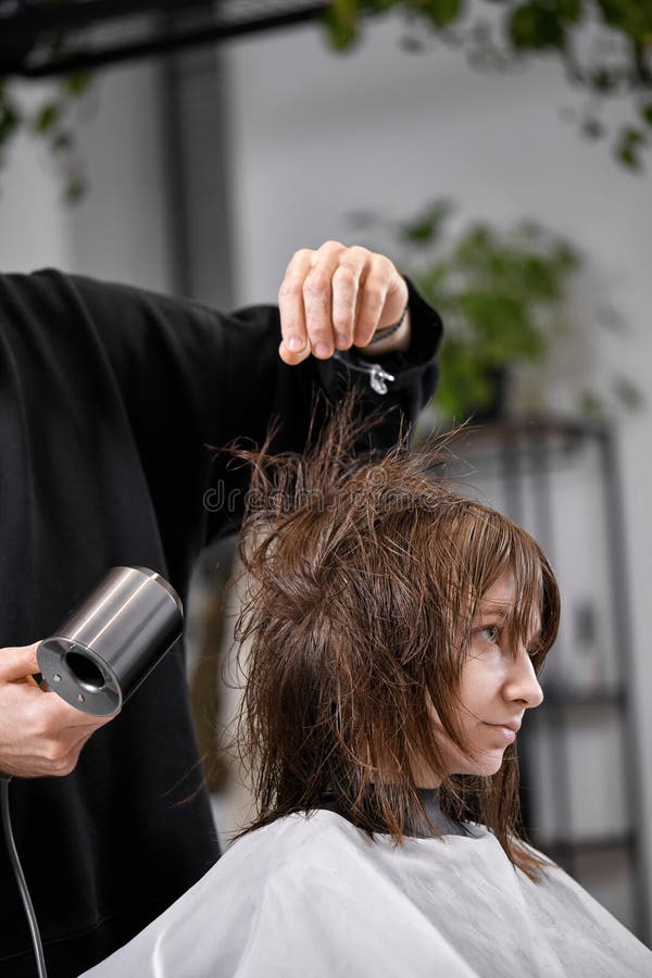 Cabeleireiro seca o cabelo com uma mulher de secador de cabelo no