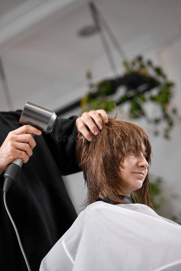 Cabeleireiro seca e modela o cabelo com um secador de cabelo no salão de  beleza