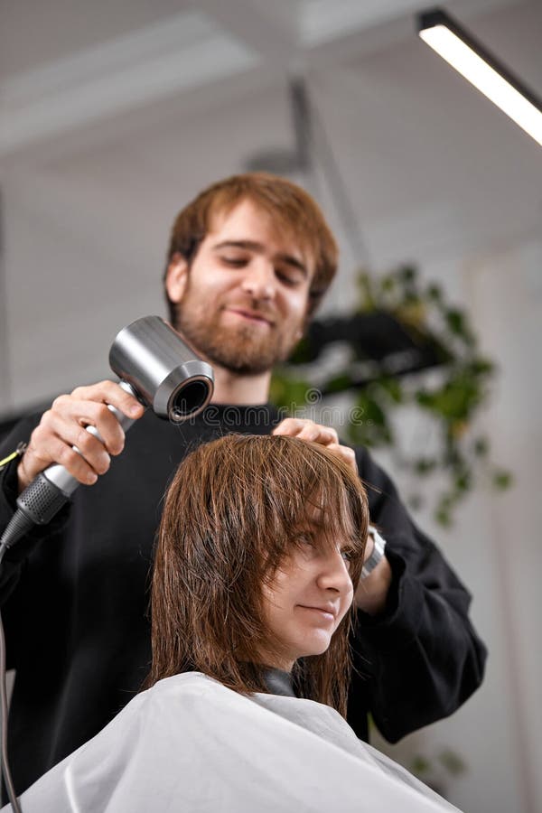 Cabeleireiro seca e modela o cabelo com um secador de cabelo no salão de  beleza