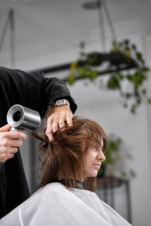 Cabeleireiro seca e modela o cabelo com um secador de cabelo no salão de  beleza