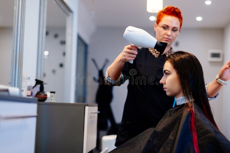 Cabeleireiro seca o cabelo com uma mulher de secador de cabelo no