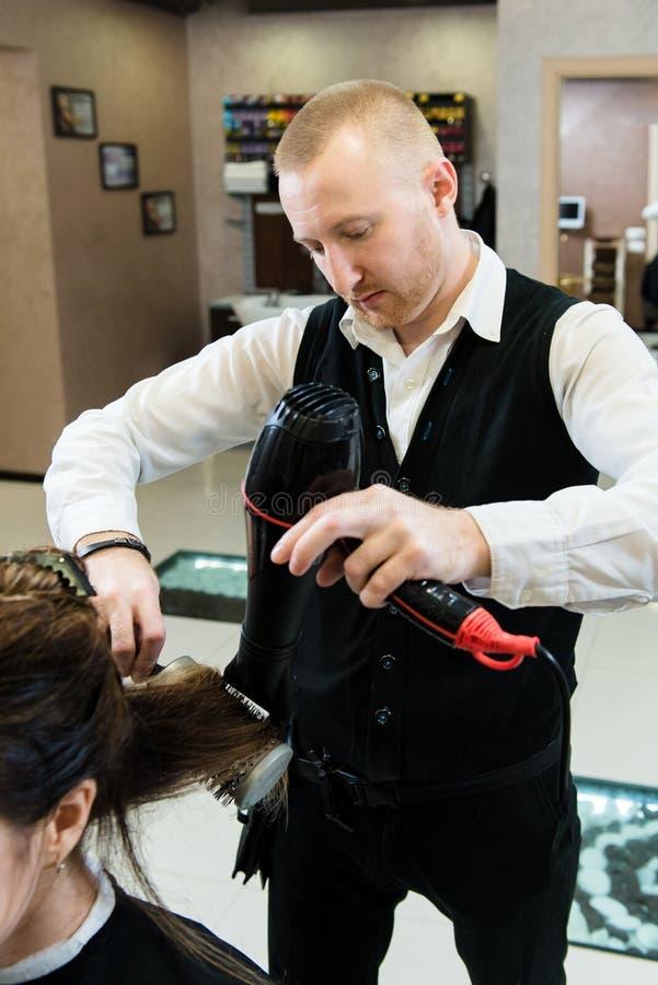 Cabeleireiro seca o cabelo com uma mulher de secador de cabelo no