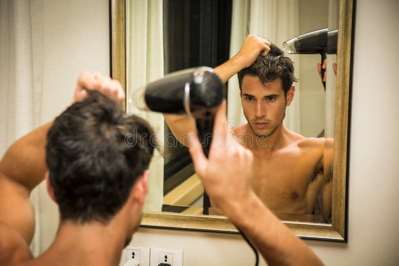 Cabello seco descamisado del hombre joven con el hairdryer imagen de archivo Cabello seco descamisado del hombre joven con el hairdryer imagen de archivo