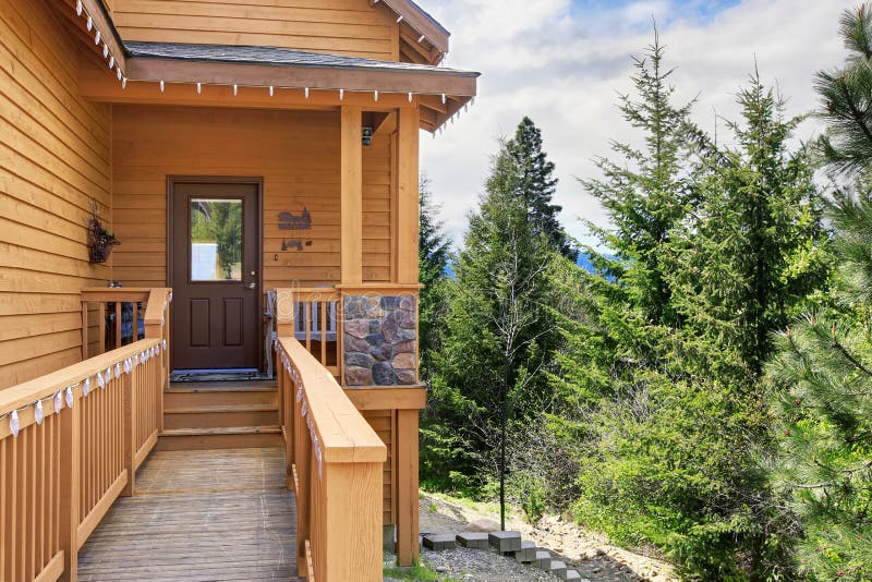 Cabin style home entrance with long walkway and railings. Wood cabin style home entrance with front door in the woods with lots of greenery royalty free stock photo Cabin style home entrance with long walkway and railings. Wood cabin style home entrance with front door in the woods with lots of greenery royalty free stock photo