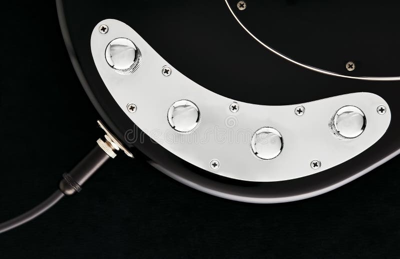 Cable jack connected to black electric bass guitar input with volume and tone control knobs royalty free stock photography
