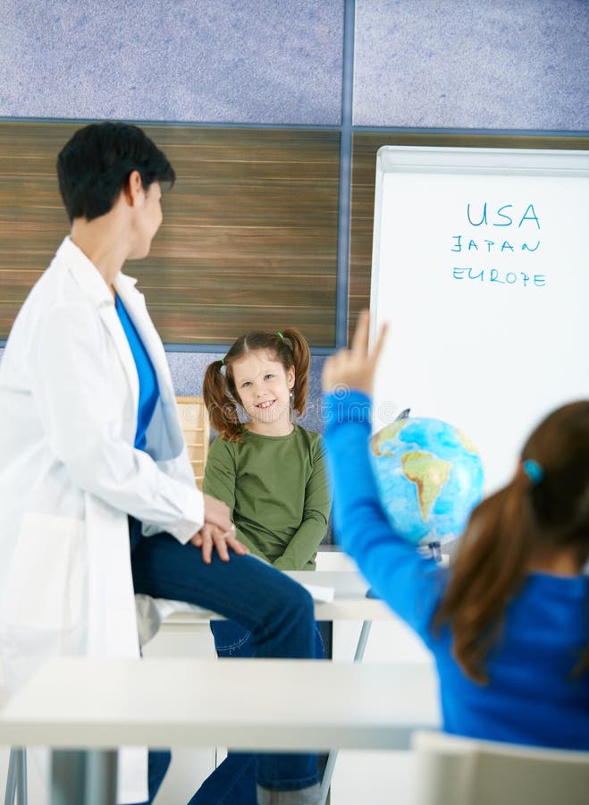 Elementary age schoolkid at lackboard looking at teacher, other girl raising hand. Elementary age schoolkid at lackboard looking at teacher, other girl raising hand.