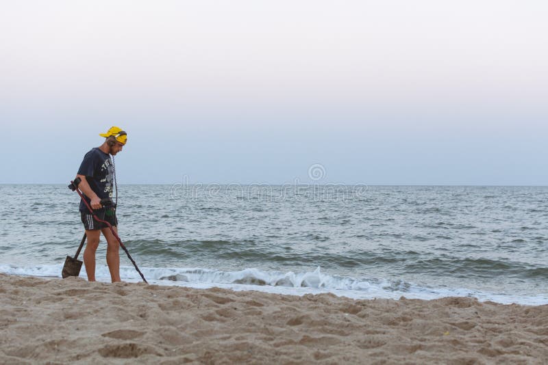 Treasure hunter with a metal detector walks along the beach of the Black Sea after sunset looking for treasure. Treasure hunter with a metal detector walks along the beach of the Black Sea after sunset looking for treasure