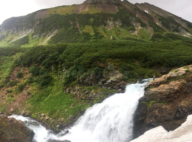 The Tahkoloch River begins in the glacier at the summit of the extinct Vachkazhets volcano and flows down to form beautiful rapids and one waterfall. Tourist is visible on the top of waterfall. The Tahkoloch River begins in the glacier at the summit of the extinct Vachkazhets volcano and flows down to form beautiful rapids and one waterfall. Tourist is visible on the top of waterfall.