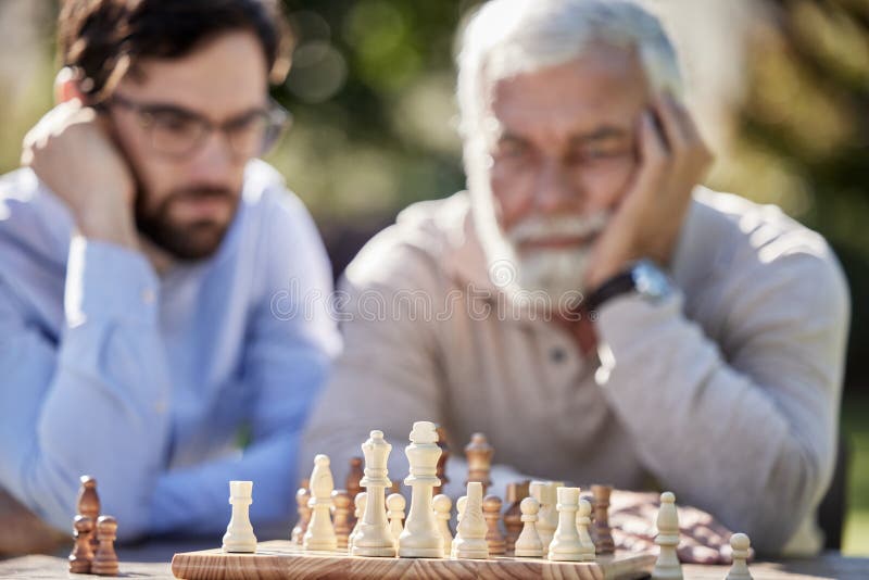Amigos de xadrez e jogos de tabuleiro na mesa de madeira pensando em  movimento estratégico ou tático em casa grupo sênior de homens jogando e  segurando ou movendo a peça branca para