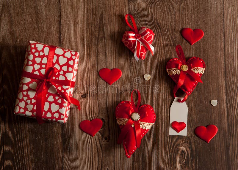 The Concept Of Valentine`s Day. Gift boxes and hand sewn textile decorative red hearts with silk ribbons on wooden background. The Concept Of Valentine`s Day. Gift boxes and hand sewn textile decorative red hearts with silk ribbons on wooden background.