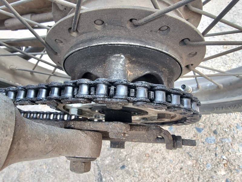 Cadena de rueda trasera y piñón de motocicleta sucia. Un disparo de cierre centrado en la cadena de la rueda trasera y en el piñón de una motocicleta. Los componentes muestran signos de uso con suciedad y suciedad acumuladas