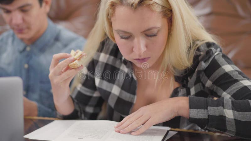 Caderno louro bonito da leitura da menina do retrato que come o sanduíche quando sua informação de exploração do noivo no Interne