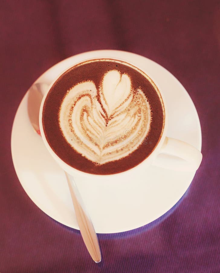 Caf? chaud de cappuccino d?cor? de l'art de floraison de mousse de fleur sur la mousse cuite ? la vapeur de lait dans la tasse bl image stock Caf? chaud de cappuccino d?cor? de l'art de floraison de mousse de fleur sur la mousse cuite ? la vapeur de lait dans la tasse bl image stock
