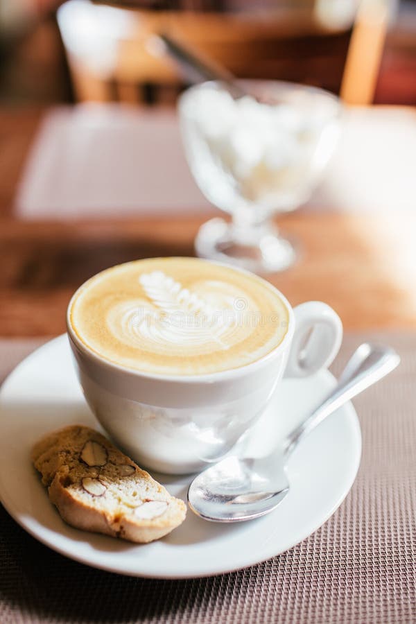 Caffè caldo del Latte di arte in una tazza con il biscotti sul fondo di legno della sfuocatura della caffetteria e della tavola c fotografia stock libera da diritti Caffè caldo del Latte di arte in una tazza con il biscotti sul fondo di legno della sfuocatura della caffetteria e della tavola c fotografia stock libera da diritti