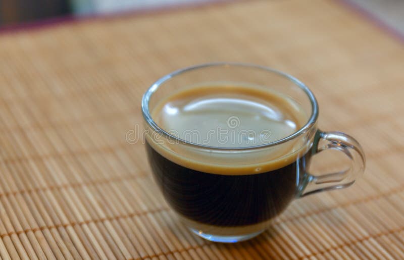 Caffè del caffè espresso con il crema fine-bollito dorato visto da sopra dentro una tazza cristallina sul supporto di bambù del p