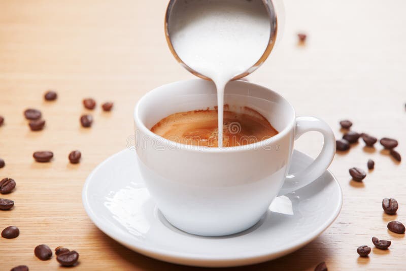 Adding milk to a cup of coffee with coffee beans spread around. Adding milk to a cup of coffee with coffee beans spread around.