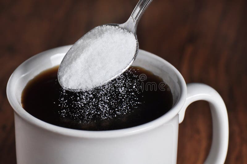 Black coffee in a white cup with granulated sugar being poured from a spoon. Black coffee in a white cup with granulated sugar being poured from a spoon