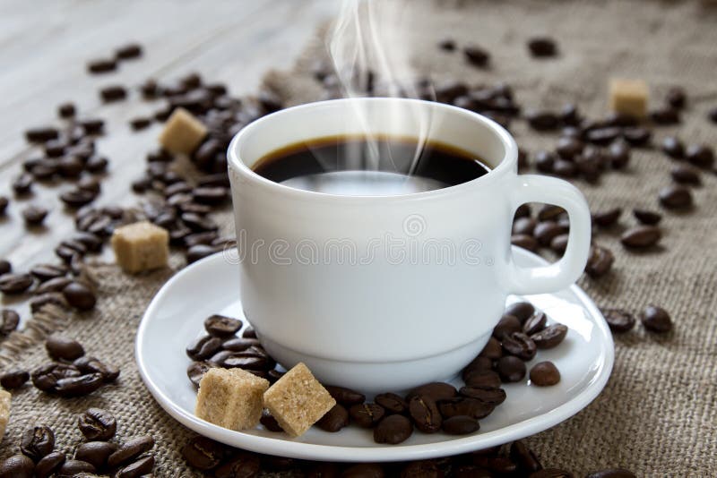 Caffè nero caldo in una tazza bianca, in uno zucchero di canna e nei semi di cacao torrefatti fotografie stock