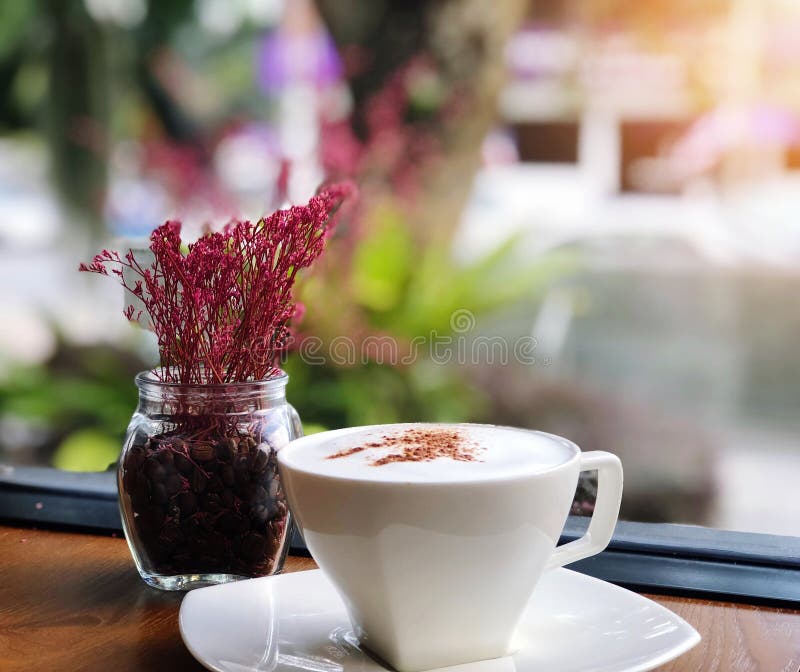Café caliente en una taza blanca en la tabla y el florero de madera en fondo de la falta de definición de la cafetería imágenes de archivo libres de regalías Café caliente en una taza blanca en la tabla y el florero de madera en fondo de la falta de definición de la cafetería imágenes de archivo libres de regalías