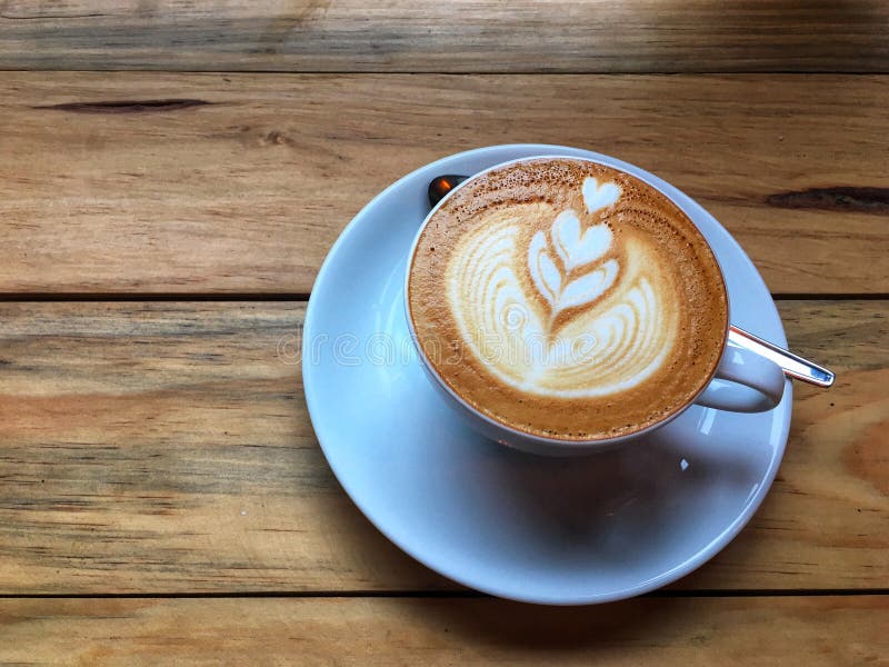 Café chaud de cappuccino dans la tasse et soucoupe blanche avec la cuillère sur le fond en bois de table Art du dessin de mousse