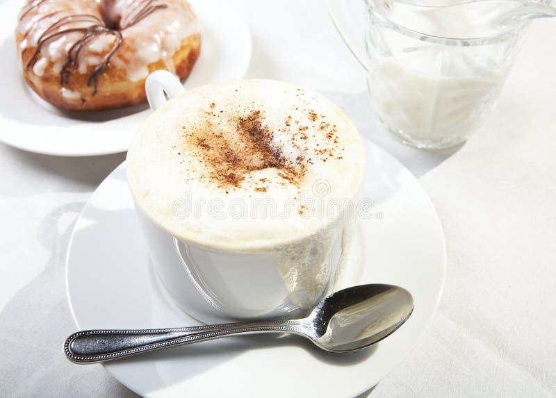 Coffee cup with magnificent milk foam and cinnamon dressing and donut in background. Coffee cup with magnificent milk foam and cinnamon dressing and donut in background