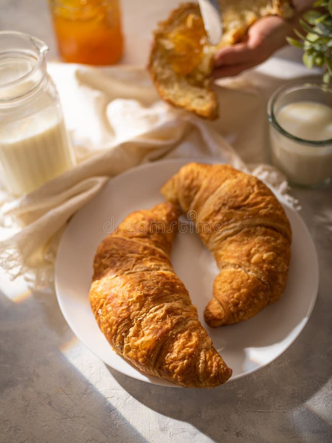 Morning breakfast. Poor background, white dishes. Two croissants with a golden crust. There is milk in a glass and a jug. Close-up. Pastel shades.Beautiful still life. No people. Morning breakfast. Poor background, white dishes. Two croissants with a golden crust. There is milk in a glass and a jug. Close-up. Pastel shades.Beautiful still life. No people.