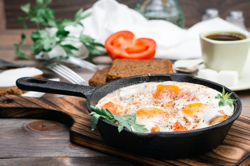 Café da manhã pronto: shakshuka dos ovos fritos com tomates e salsa em uma bandeja, no pão com manteiga e no café imagem de stock Café da manhã pronto: shakshuka dos ovos fritos com tomates e salsa em uma bandeja, no pão com manteiga e no café imagem de stock