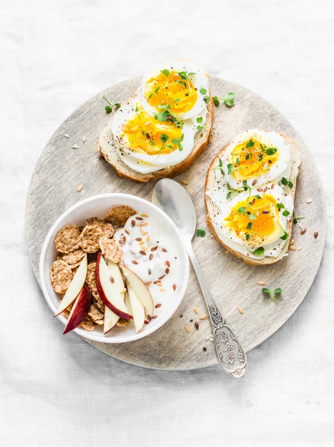 Healthy breakfast - sandwiches with cream cheese and boiled egg, yogurt with apple and flax seeds on light background, top view. Healthy breakfast - sandwiches with cream cheese and boiled egg, yogurt with apple and flax seeds on light background, top view