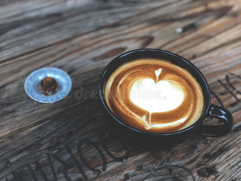 Café del arte del Latte del amor del corazón en taza negra en la tabla de madera del vintage Amante del caf? imagen de archivo libre de regalías Café del arte del Latte del amor del corazón en taza negra en la tabla de madera del vintage Amante del caf? imagen de archivo libre de regalías