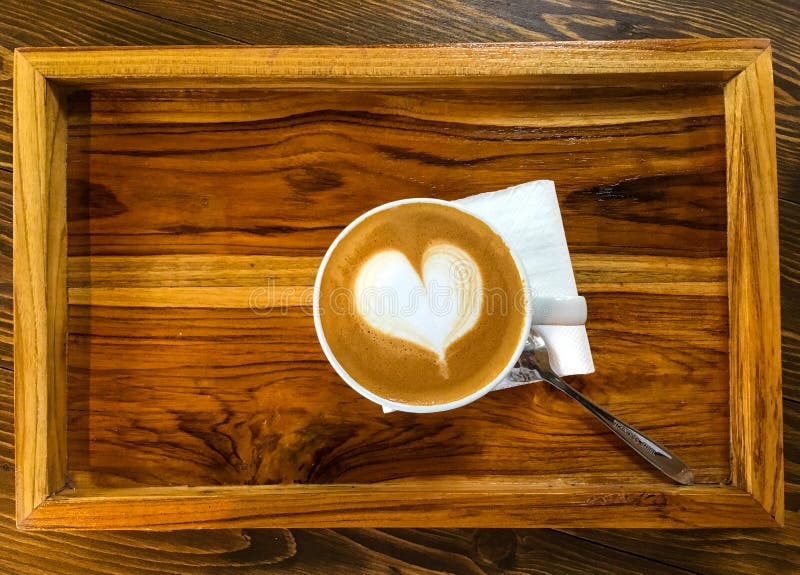 Café del Latte con espuma de la leche de la corazón-forma en la bandeja de madera en café