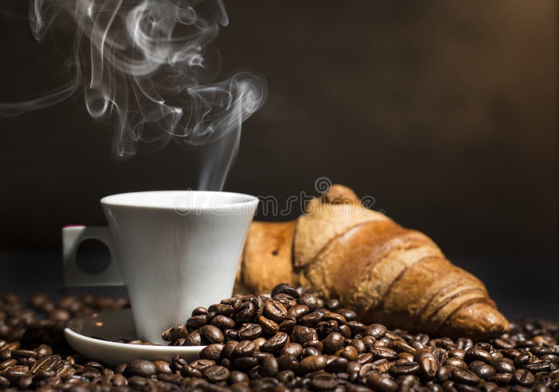 Coffee in a white cup and croissant on coffee beans background. Coffee in a white cup and croissant on coffee beans background