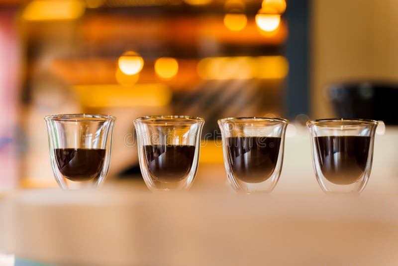 4 Flavored coffee close-up espresso in double glass cup with blurred background. Macro photo of coffee on the wooden table in loft style cafe. 4 Flavored coffee close-up espresso in double glass cup with blurred background. Macro photo of coffee on the wooden table in loft style cafe