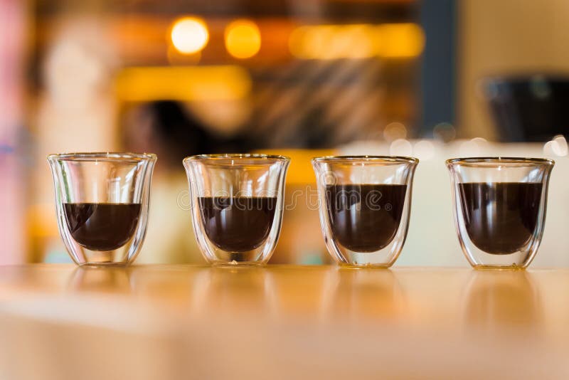 4 Flavored coffee close-up espresso in double glass cup with blurred background. Macro photo of coffee on the wooden table in loft style cafe. 4 Flavored coffee close-up espresso in double glass cup with blurred background. Macro photo of coffee on the wooden table in loft style cafe