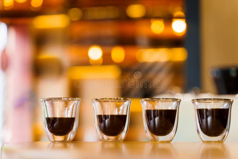 4 Flavored coffee close-up espresso in double glass cup with blurred background. Macro photo of coffee on the wooden table in loft style cafe. 4 Flavored coffee close-up espresso in double glass cup with blurred background. Macro photo of coffee on the wooden table in loft style cafe