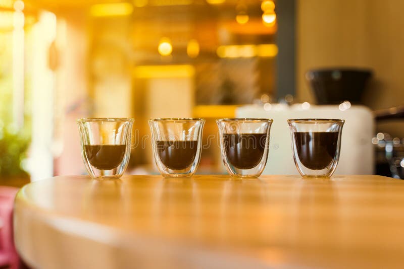 4 Flavored coffee espresso in double glass cup with sun light on background in cafe. Coffee on the wooden table with blurred background. 4 Flavored coffee espresso in double glass cup with sun light on background in cafe. Coffee on the wooden table with blurred background