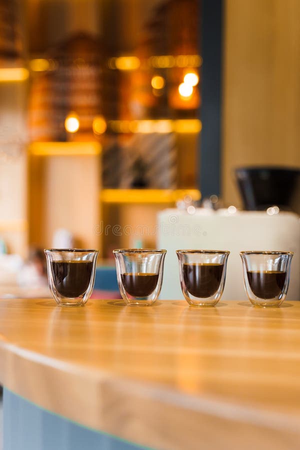 4 Flavored coffee espresso in double glass cup with sun light on background in cafe. Coffee on the wooden table with blurred background. 4 Flavored coffee espresso in double glass cup with sun light on background in cafe. Coffee on the wooden table with blurred background.